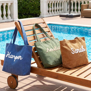 Lifestyle display of five personalized corduroy tote bags featuring raised custom name embroidery. The roomy zippered shoulder bags are shown in navy blue, dark green, white, brown and pink.